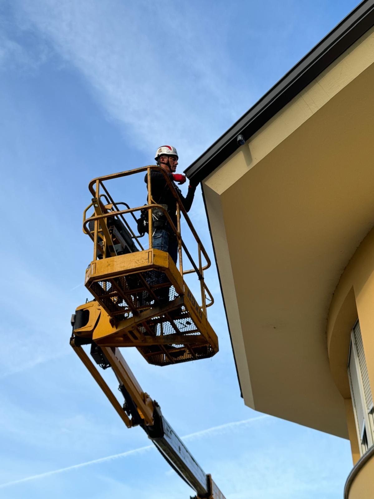 Instalador con casco y arnés en la cesta de una plataforma articulada junto al alero de una vivienda