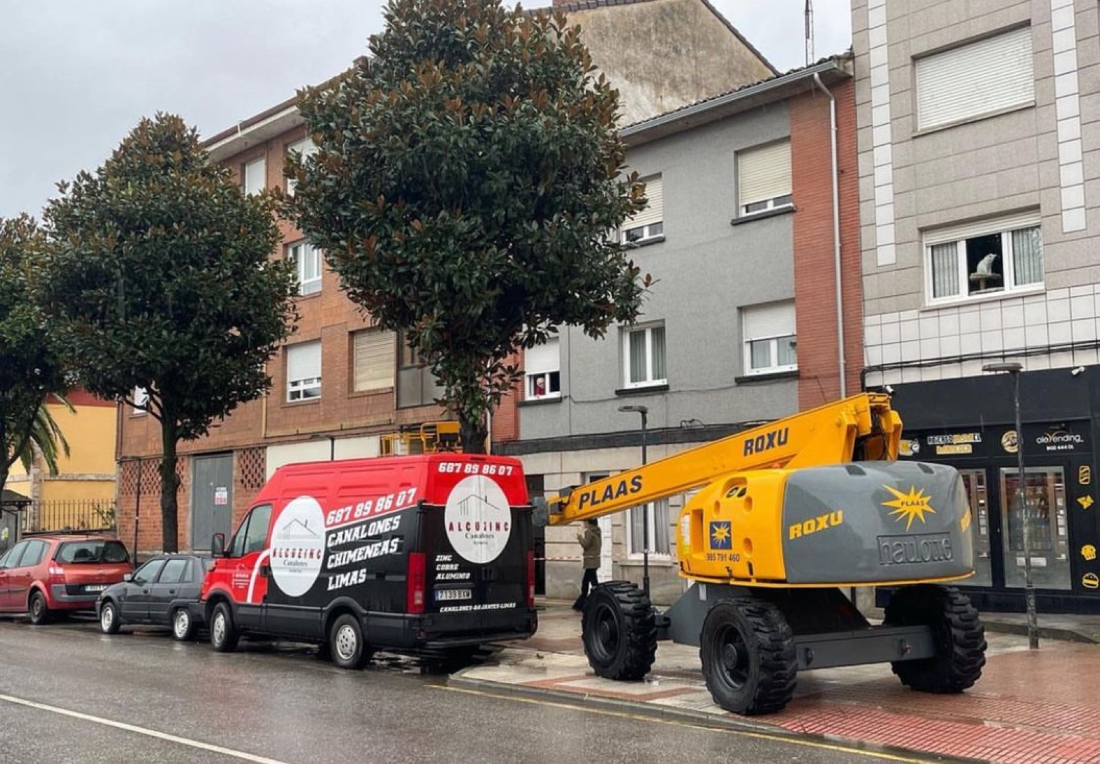 Furgoneta roja de ALCUZINC aparcada frente a un edificio, con la plataforma articulada detrás