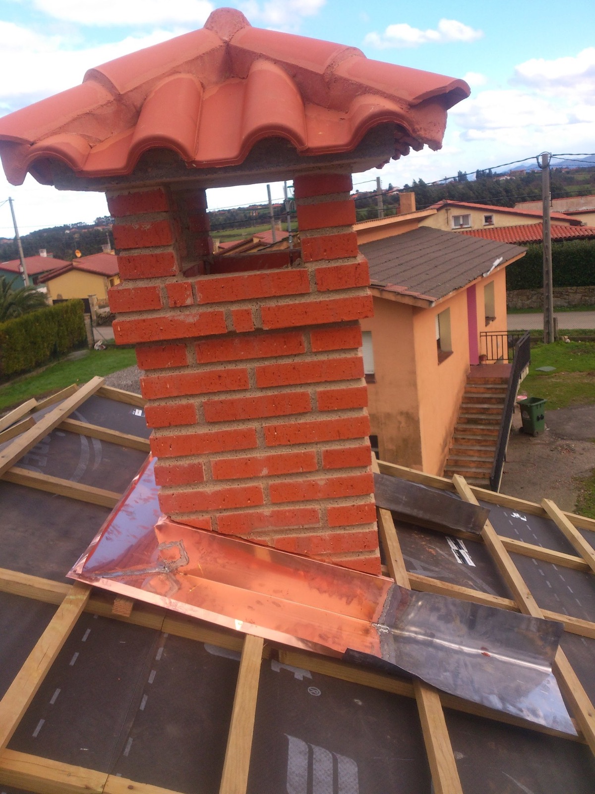 Lima de cobre alrededor de una chimenea de ladrillo en una cubierta en obra