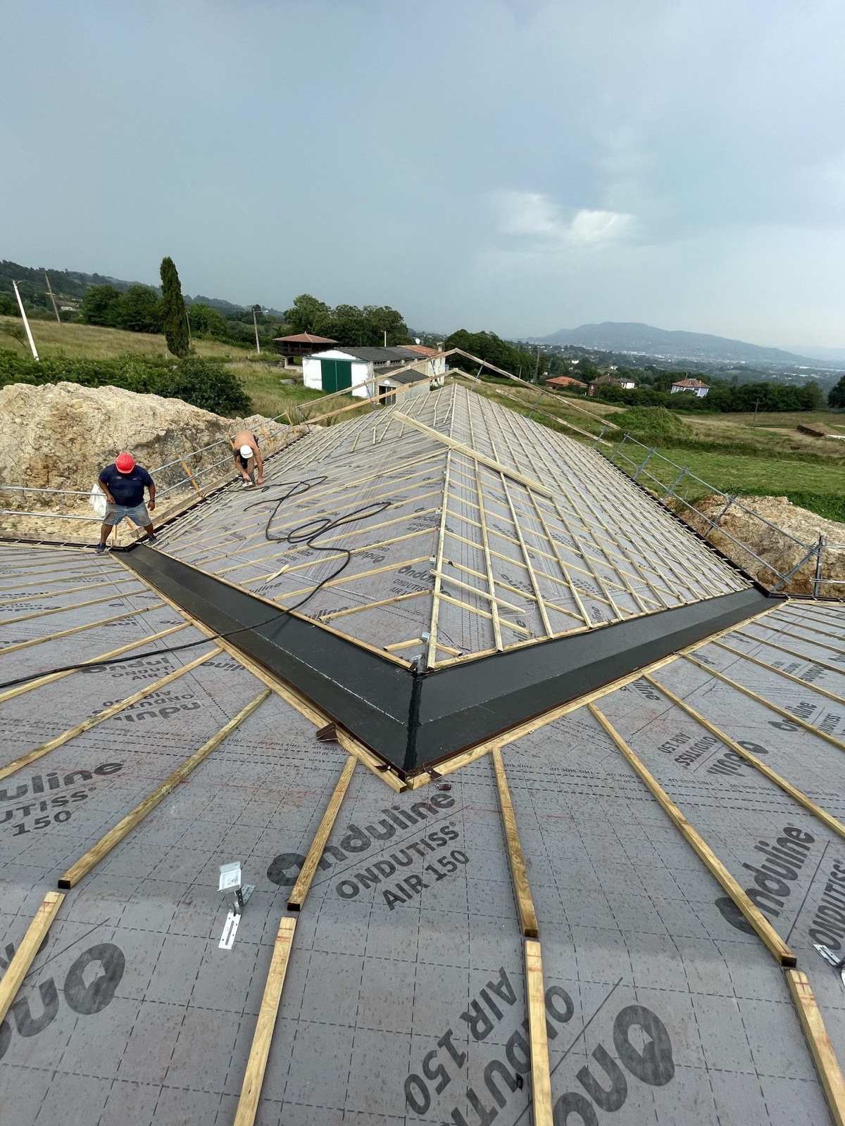 Limahoya de aluminio lacado negro instalada en una cubierta nueva de gran tamaño, con dos operarios y el paisaje asturiano al fondo