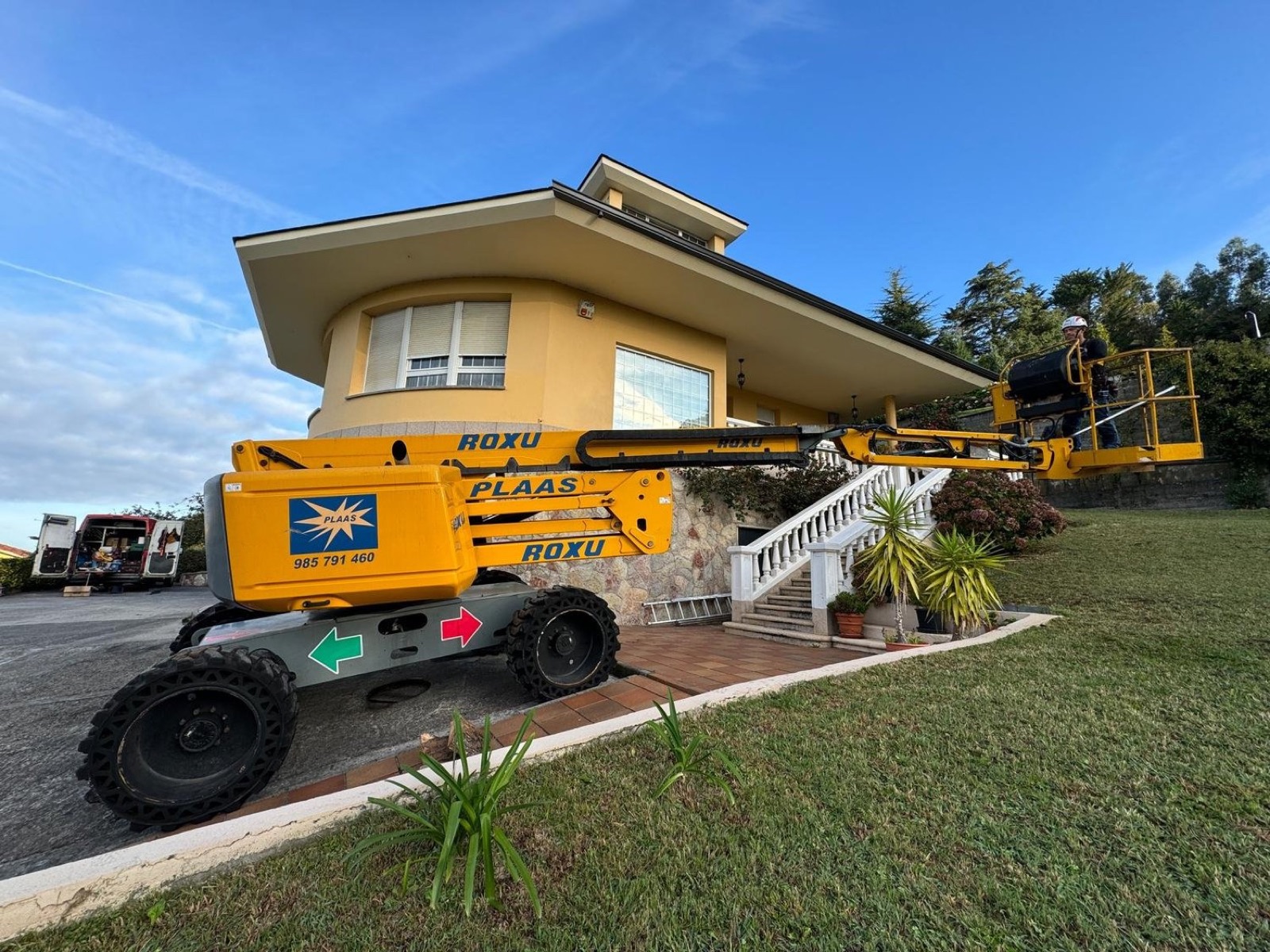 Plataforma articulada amarilla desplegada frente a un chalet al amanecer, con el instalador en la cesta